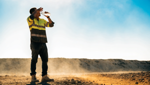 An outdoor worker in a hi-visibility shirt cooling off and drinking water on a hot, sunny job site under a bright summer sky