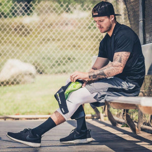 Athlete sitting on a bench applying a DonJoy cold therapy wrap to his knee