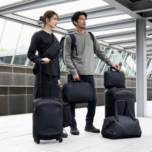 Two people standing with various Thule black luggage and bags in a transit area