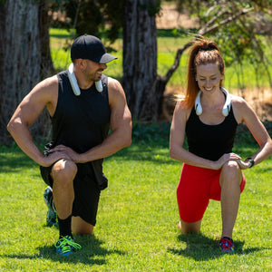 Man and woman wearing AlphaCool neck fans while performing lunges on grass
