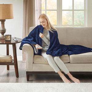 Woman sitting on a couch using a Woolrich navy blue electric heated throw blanket