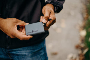 Person holding a grey ActionHeat power bank with a USB cable