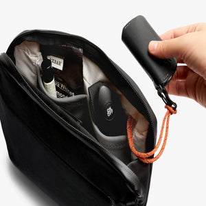 Hand placing a black Bellroy key cover into a black zippered pouch with internal pockets