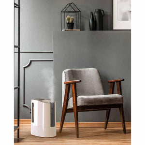 Vornado humidifier emitting mist on a wooden floor next to a grey armchair