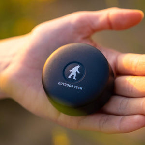 Outdoor Tech black circular wireless speaker held in palm