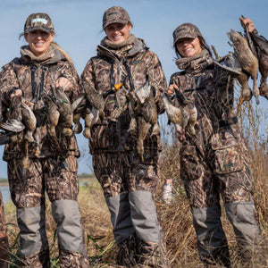 Three women wearing DSG Outerwear camouflage hunting gear holding ducks in a field
