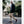Man wearing Cloud Nine Sheepskin loafers with tan trousers and a black cardigan walking on a city street