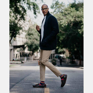 Man wearing Cloud Nine Sheepskin loafers with tan trousers and a black cardigan walking on a city street