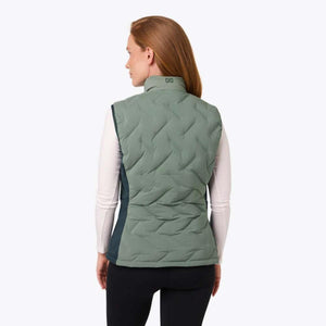 Back view of a woman wearing a sage green Mobile Warming quilted vest over a white long sleeve shirt