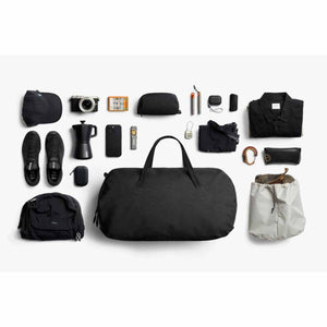 Bellroy black duffel bag surrounded by travel accessories and clothing items on a white background