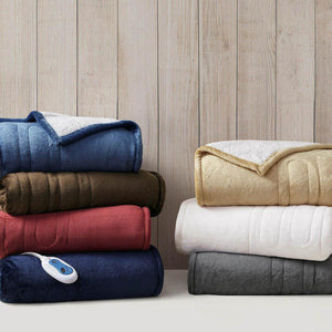 Stacks of folded Woolrich heated blankets in various colors with controllers
