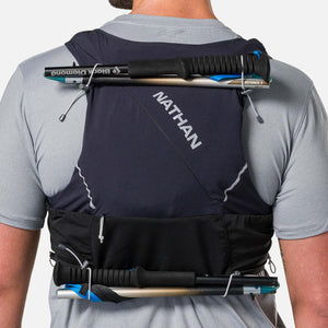 Person wearing a black Nathan hydration vest with trekking poles attached to the back