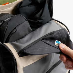Hand pulling a grey Kuhl baseball cap from a Bellroy backpack compartment