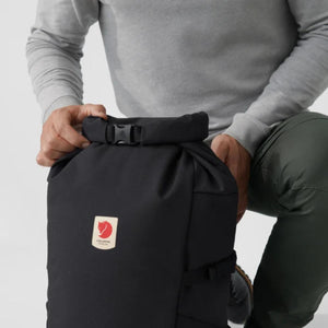 Person closing the roll top buckle on a black Fjallraven backpack
