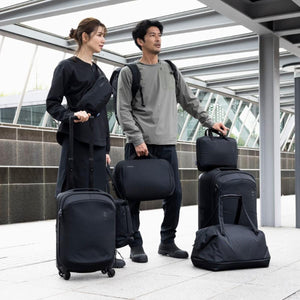 Man and woman standing with various Thule black luggage pieces and backpacks