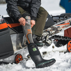 Person wearing Mobile Warming heated socks and black rubber boots while sitting on a snowmobile