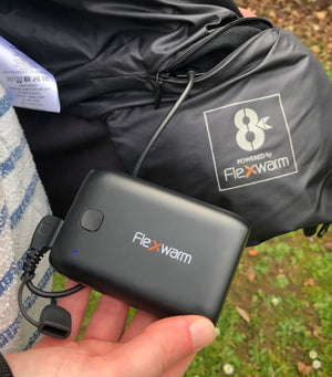 Hand holding a black Flexwarm power bank connected to a garment with a Flexwarm logo