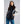 Woman wearing a black 8K FlexWarm puffer vest over a grey sweater and blue jeans