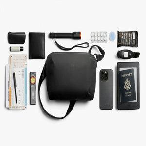 Bellroy sling bag surrounded by travel essentials including a passport, smartphone, flashlight, and snacks
