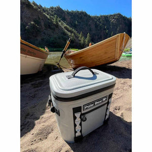 Polar Bear soft cooler on a sandy riverbank with wooden boats in the background