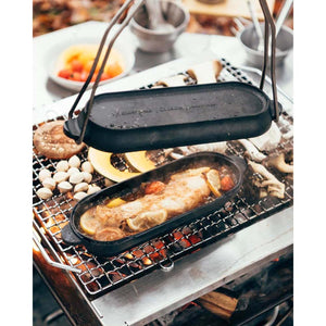 Snow Peak cast iron oval skillet cooking fish with lemon slices over a charcoal grill
