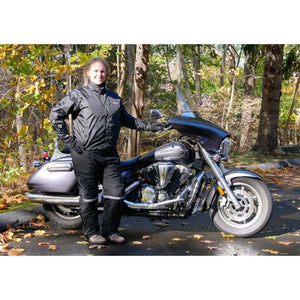 Person wearing California Heat black motorcycle gear standing next to a cruiser motorcycle in an autumn forest