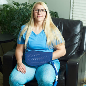 Woman sitting in a chair using a blue cold therapy wrap on her abdomen