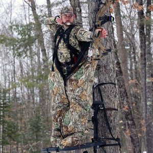 Hunter wearing camouflage suit in a tree stand aiming a compound bow