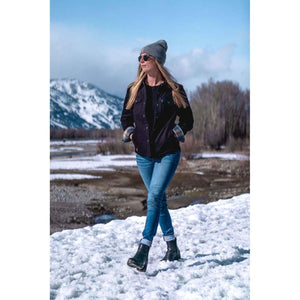 Woman wearing a Mobile Warming black jacket and beanie walking through a snowy landscape