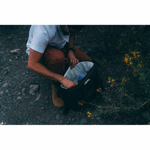 Person reaching into an open black AO Coolers backpack containing water bottles