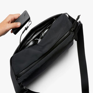 Hand holding a Bellroy key cover attached to a clip inside a black sling bag