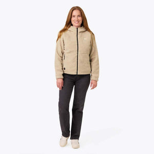 Woman wearing a beige Mobile Warming sherpa hooded jacket with a black zipper and dark jeans