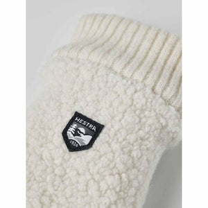 Close up of cream colored Hestra fleece mitten with ribbed cuff and brand logo patch