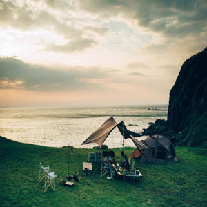 Snow Peak tent and tarp setup on a grassy cliff overlooking the ocean at sunset