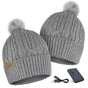 Two grey cable knit ActionHeat beanies with pom poms and a portable battery pack with charging cable