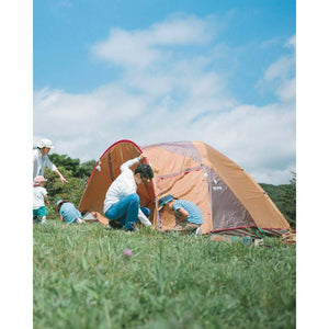 Family setting up a brown Snow Peak tent in a grassy field