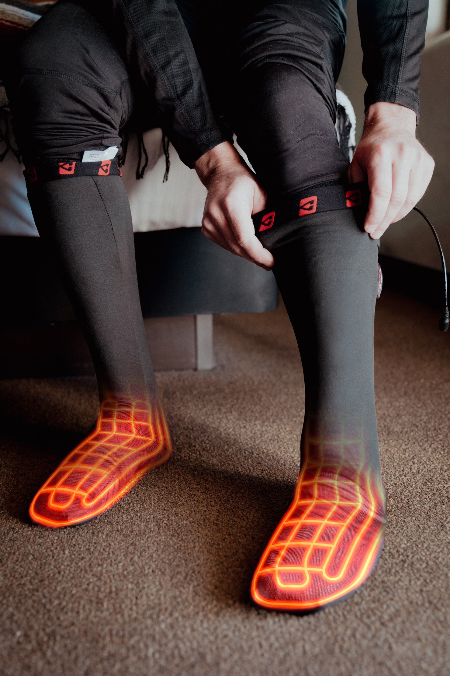 Person pulling on black heated socks with glowing red heating elements visible on the feet