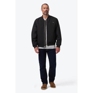 Man wearing a black Mobile Warming bomber jacket over a grey henley shirt and blue jeans