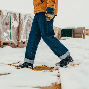 Person wearing dark blue denim jeans and black winter boots walking through snow