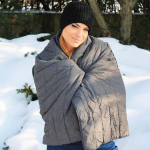 Person wearing a black beanie and wrapped in a grey ActionHeat heated blanket outdoors in the snow