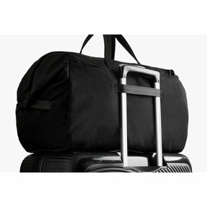 Bellroy black duffel bag secured to a rolling suitcase handle