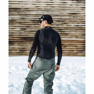 Person wearing a black POC back protector vest over a long sleeve shirt and grey ski pants in the snow
