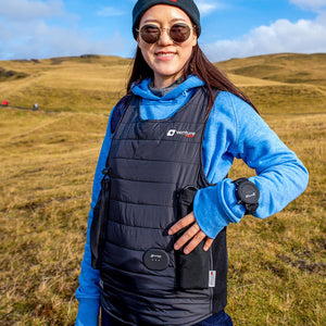 Person wearing a black Venture Heat vest over a blue hoodie in a grassy field