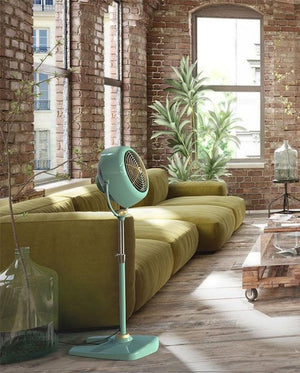 Vornado pedestal fan in mint green in a living room with brick walls
