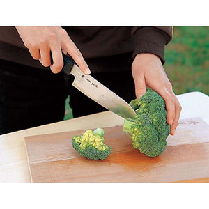 Person cutting broccoli on a wooden board with a Snow Peak knife