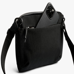 Black Bellroy crossbody bag with a smartphone partially inserted into the front zippered pocket