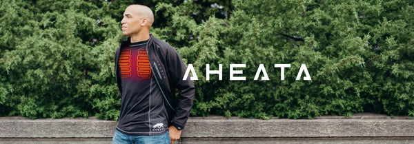 Bald man in an open black jacket over a black shirt with glowing red chest heating elements, AHEATA logo on jacket, and large 