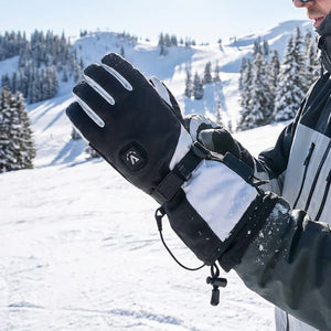 Close-up of a person's hand wearing a black and white ski glove with a white stylized logo, against a snowy mountain and pine tree landscape.