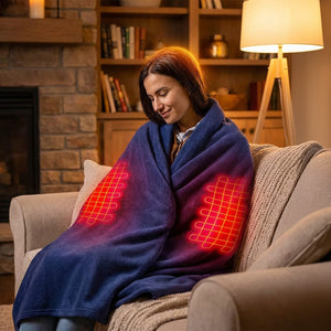 A smiling woman on a sofa wrapped in a blue heated blanket with glowing red coils visible on her lap, in a cozy living room.