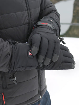A person in a black padded jacket and black heated gloves, displaying a red 'action Heat' logo, power buttons, and touchscreen fingertips, against a blurry winter backdrop.